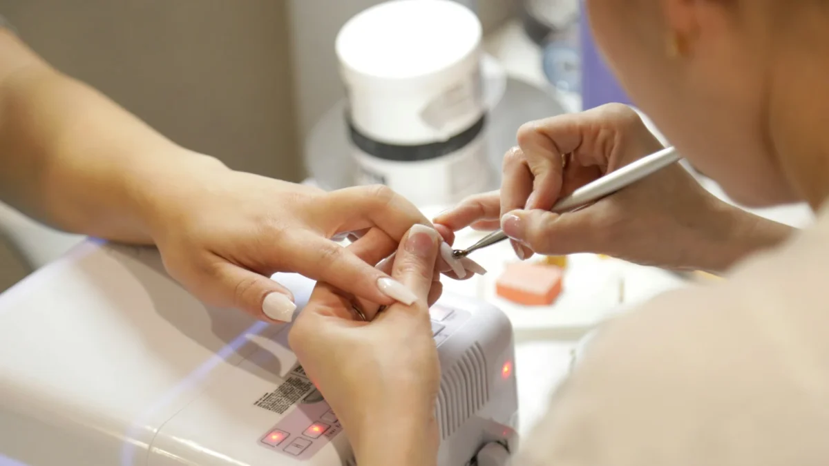 Nail technician painting a client's nails at a manicure table with polish bottles nearby, picking the best booking app for nail salons