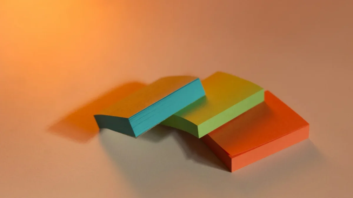 Blue, green and orange sticky note pads in warm light, the paper version of the best task management app for small business