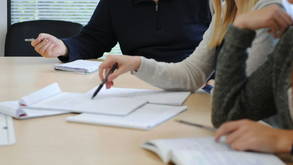 People at a meeting table with notebooks and papers, one pointing with a pen, a session of HR consulting for startups