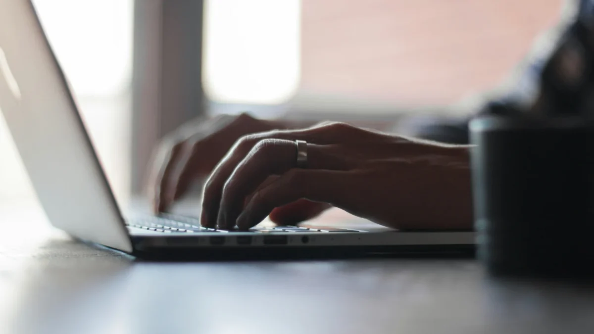 Close view of hands typing on a laptop at a table in soft light, a founder comparing HR tools for small business