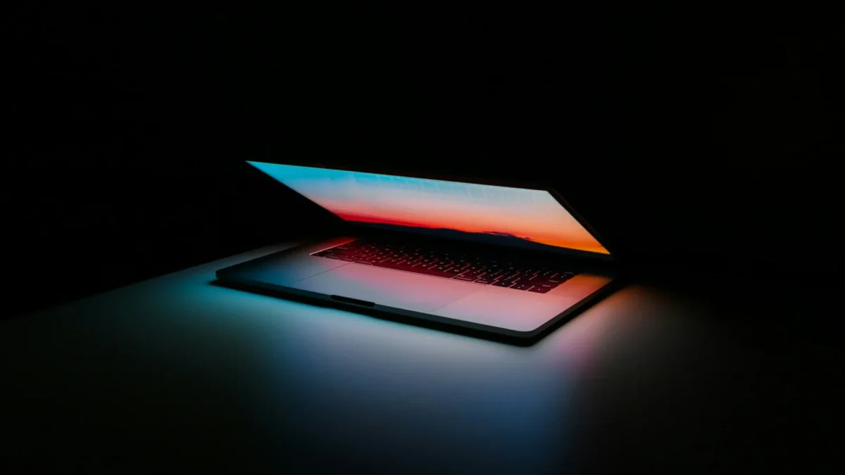 Half-open laptop glowing with colour in a dark room, ready to set up with an information technology onboarding checklist